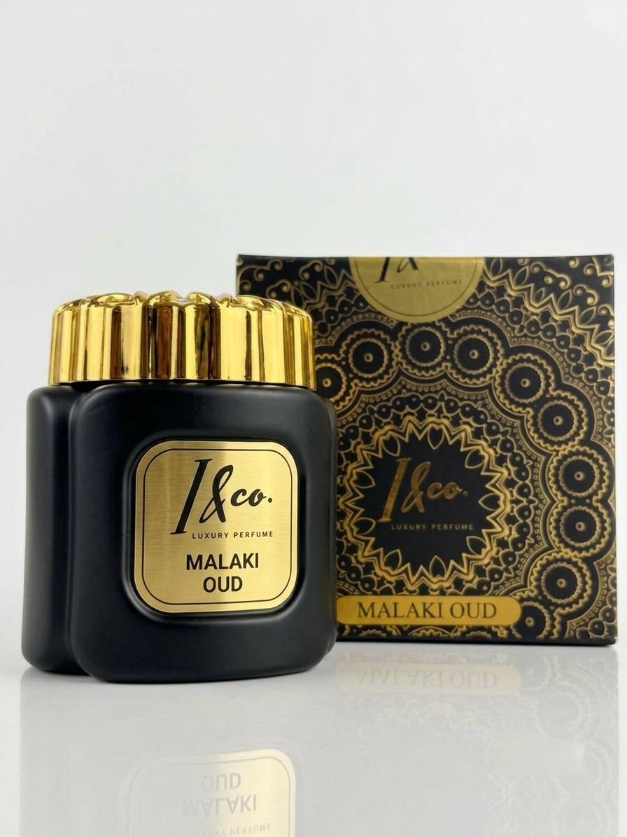 A bottle of 1&co. Malaki Oud luxury perfume in a black glass jar with a gold cap and gold label, shown next to its black and gold patterned outer box on a reflective white surface.