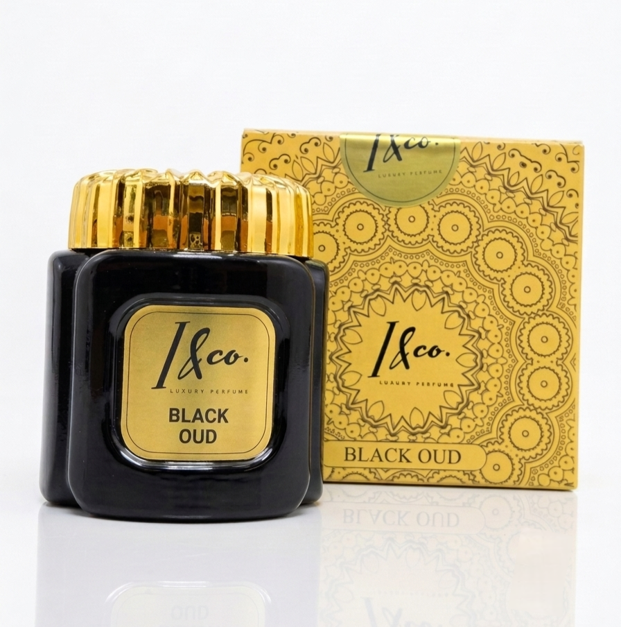 A bottle of 1&Co. Luxury Fragrances Black Oud perfume next to its ornate gold patterned box, set against a clean white background with a subtle reflection.