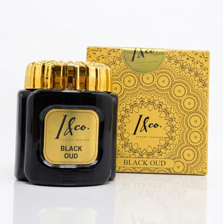A bottle of 1&Co. Luxury Fragrances Black Oud perfume next to its ornate gold patterned box, set against a clean white background with a subtle reflection.